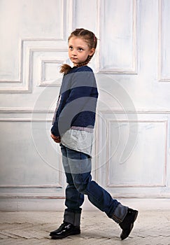 Happy fun smiling kid girl posing in fashion blue jeans, blouse, black boots and jacket on studio background. Full length