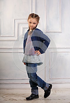 Happy fun smiling kid girl posing in fashion blue jeans, blouse, black boots and jacket on studio background. Full length