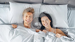 Happy and Fun Young Couple Lying under Blanket on a Bed, Making Silly Faces and Laughing. Lovely Y