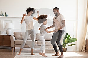 Happy funny active african family with daughter dancing at home