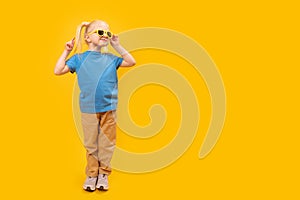 Happy funny blond little girl wear sunglasses and blue t-shirt on yellow background. Copy space, mock up