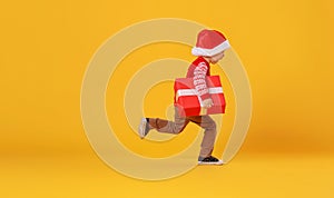 Happy funny child boy in red  running with Christmas gift on yellow background