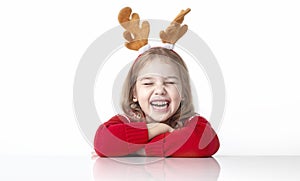 Happy funny child girl in christmas costume sitting at white empty space table. Holiday advertising blank