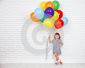 Happy funny child girl with colorful balloons near an brick wal