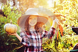Happy funny child girl in farmer hat and shirt playing and picking autumn vegetable harvest