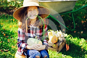 happy funny child girl in farmer hat and shirt playing and picking autumn vegetable harvest