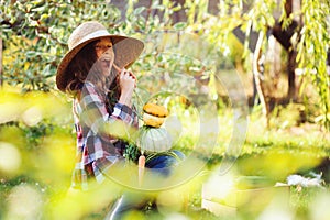 Happy funny child girl in farmer hat and shirt playing and picking autumn vegetable harvest in sunny garden