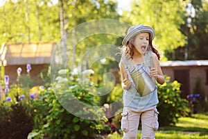 Happy funny child girl in gardener hat playing with watering can