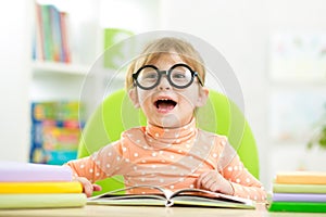 Happy funny child girl in glasses reading a book