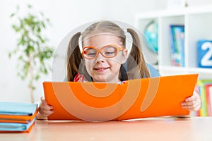 Happy funny child girl in glasses reading a book