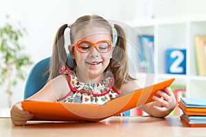 Happy funny child girl in glasses reading a book