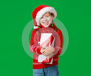 Happy funny child girl in red Christmas hat   with gift on green   background