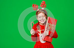 Happy funny child girl in red Christmas reindeer costume with gift on green   background