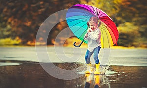 Happy funny child girl with umbrella jumping on puddles in rubb