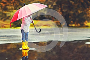 Happy funny child girl with umbrella jumping on puddles in rubb