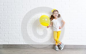 Happy funny child girl with yellow balloon near an empty wall