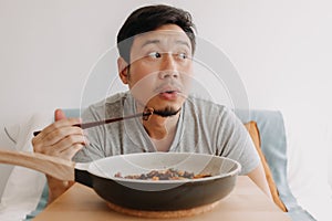 Happy funny face of man eating homemade food in the pan with chopsticks.