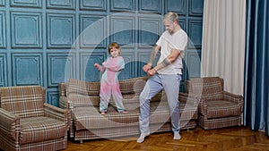 Happy funny family father and child kid daughter dancing, jumping on sofa, listening music at home