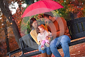 Happy funny family with red umbrella under the autumn shower