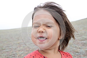 Happy funny girl with expression portrait. Wind is blowing. Smiling without teeth little child. Having fun
