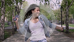 Happy funny girl walking down the street and dancing while listening to music on headphones