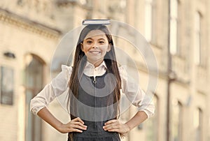 Happy funny kid with long hair in school uniform hold study book on head outdoors, bibliophile