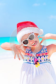 Happy funny little girl in Santa hat during Christmas beach vacation have a lot of fun