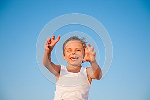 Happy funny little kid in white tank top on blue sky background with copy space