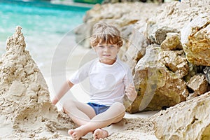 Happy funny little preschool kid boy having fun with building a sand castle on ocean beach. child playing on family