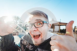 Happy funny man holds house keys on house shaped keychain in front of a new home