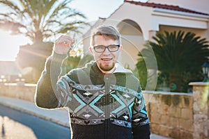 Happy funny man holds house keys on house shaped keychain in front of a new home