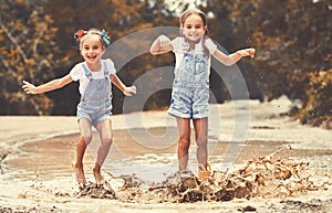 Happy funny sisters twins child by girl jumping on puddles and laughing