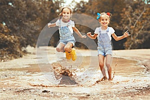 Happy funny sisters twins child girl jumping on puddles in rub
