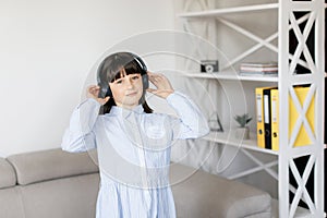 Happy funny teen girl with dark hair wear headphones standing in room and listening new pop music, enjoying, singing song,