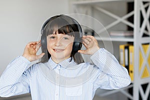 Happy funny teen girl with dark hair wear headphones standing in room and listening new pop music, enjoying, singing song,