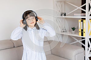 Happy funny teen girl with dark hair wear headphones standing in room and listening new pop music, enjoying, singing song,