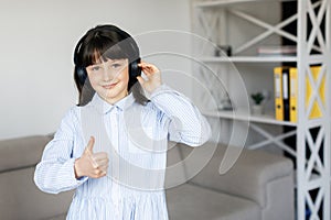 Happy funny teen girl with dark hair wear headphones standing in room and listening new pop music, enjoying, singing song,