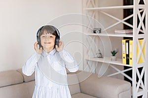 Happy funny teen girl with dark hair wear headphones standing in room and listening new pop music, enjoying, singing song,