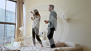 Happy funny young family couple dancing jumping on bed mattress