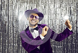 Happy funny young guy wearing purple jacket, hat and sunglasses dancing at party