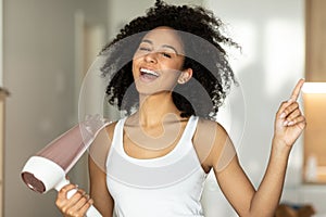 Happy funny young woman indoors at home in bathroom dry hair with hair dryer singing.