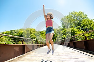 Happy and funny young woman jumping on a bridge in a sunny day