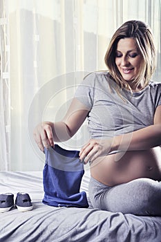 Happy future mommy showing unborn baby boy suit