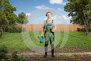 Happy gardener with a watering can and a flower pot standing in a green backyard