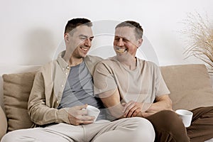 Happy gay couple with casual clothes spending time together at home, watching movie on the laptop and drinking tea. Two