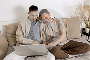 Happy gay couple with casual clothes spending time together at home and watching movie on the laptop. Two caucasian men