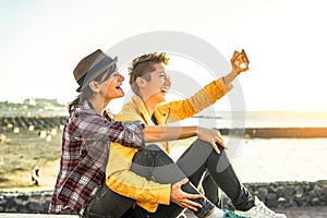 Happy gay couple taking a selfie with mobile smart phone camera on the beach at sunset - Lesbians having fun in holiday