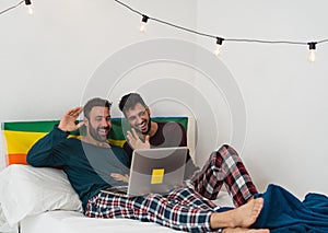 Happy gay men couple doing video call using laptop inside bed
