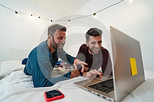 Happy gay men couple using laptop in bed