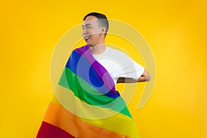 Happy gay with pride movement LGBT Rainbow flag on shoulder isolated yellow background. Man with a gay pride flag